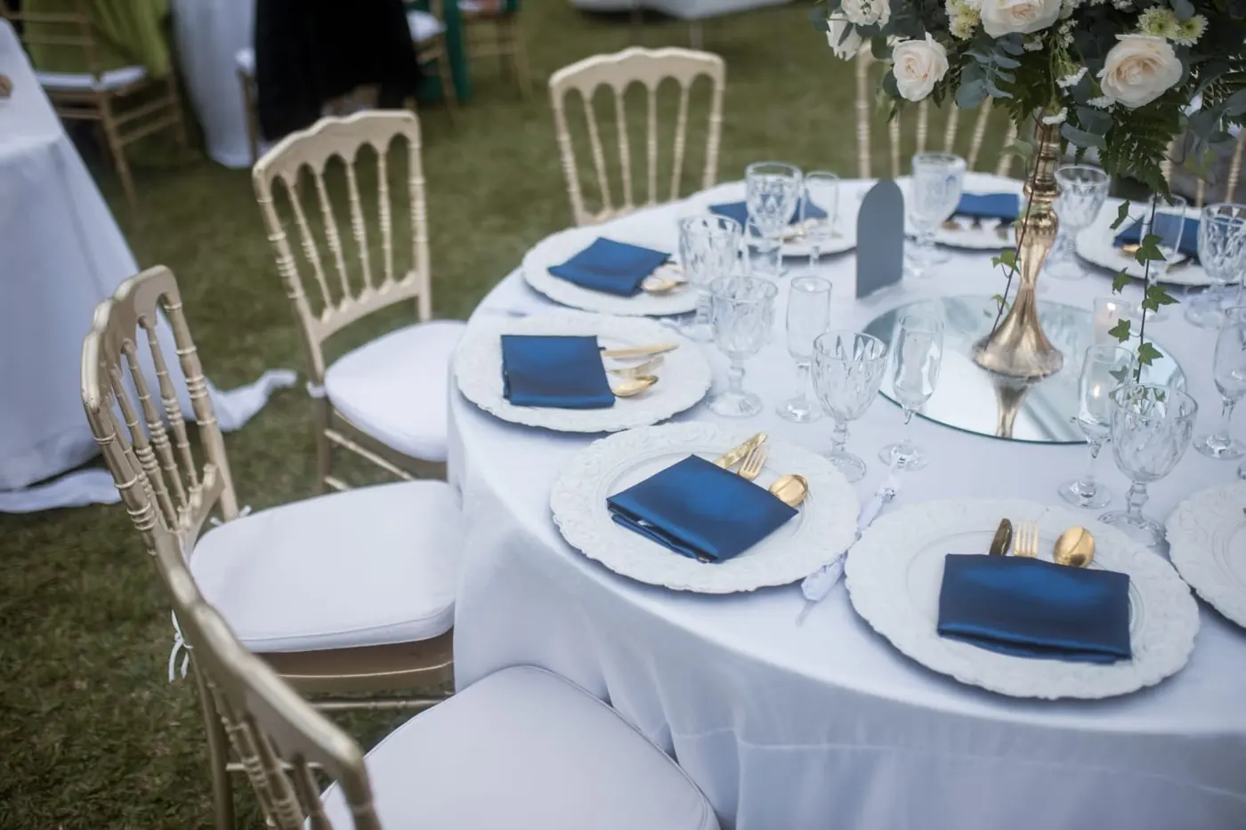 Mesa redonda de invitados con vajilla azul, detalles dorados y centro floral